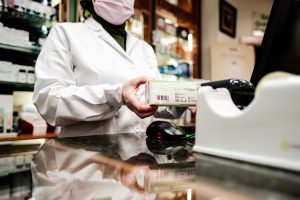 A pharmacist scans a box of medicines behind a pharmacy counter